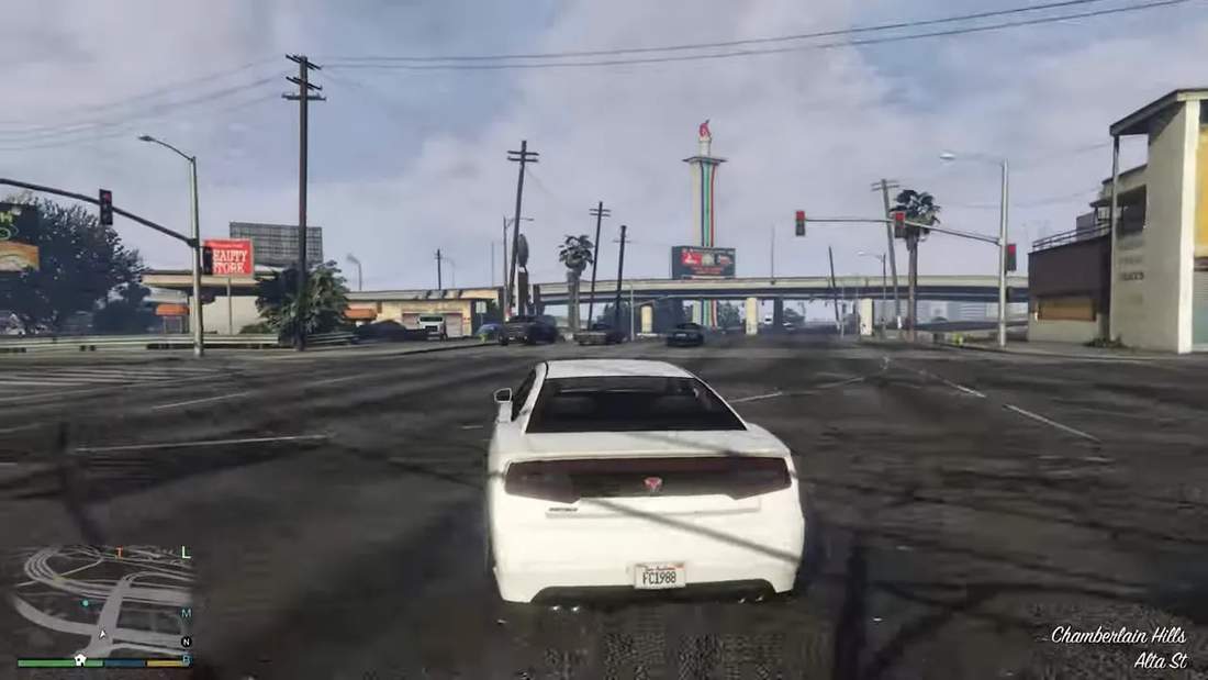 GTA V third-person driving view of a white car on a Los Santos street with city landmark in the distance