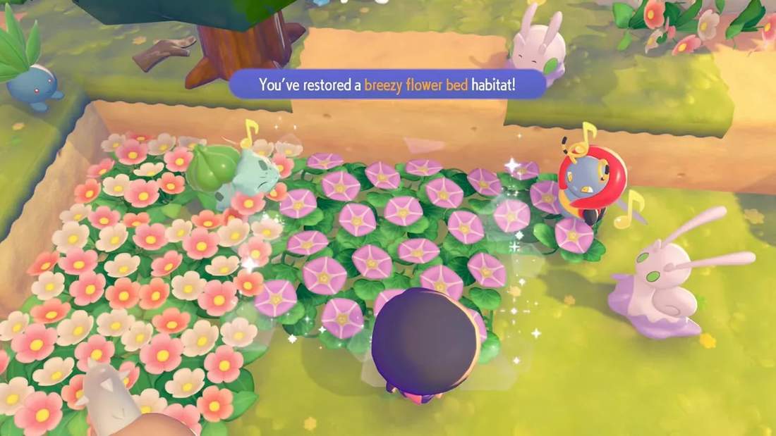 Game UI message 'You've restored a breezy flower bed habitat' over a 3x3 bed of pink and purple seashore flowers with Bulbasaur nearby