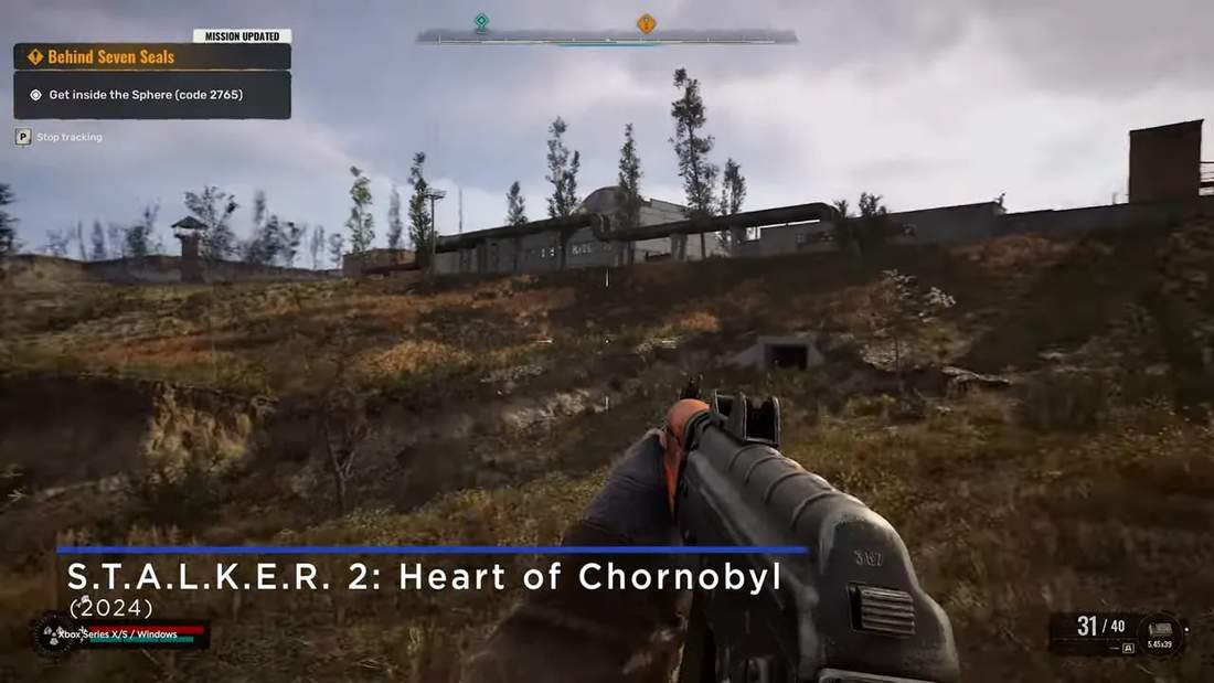 First-person view approaching an industrial compound in a grassy wasteland with weapon HUD and title overlay for S.T.A.L.K.E.R. 2.