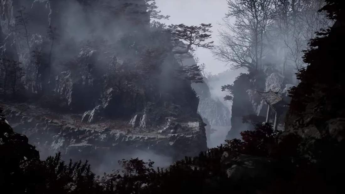 Mist fills a deep ravine between wooded cliffs with a small structure on the right